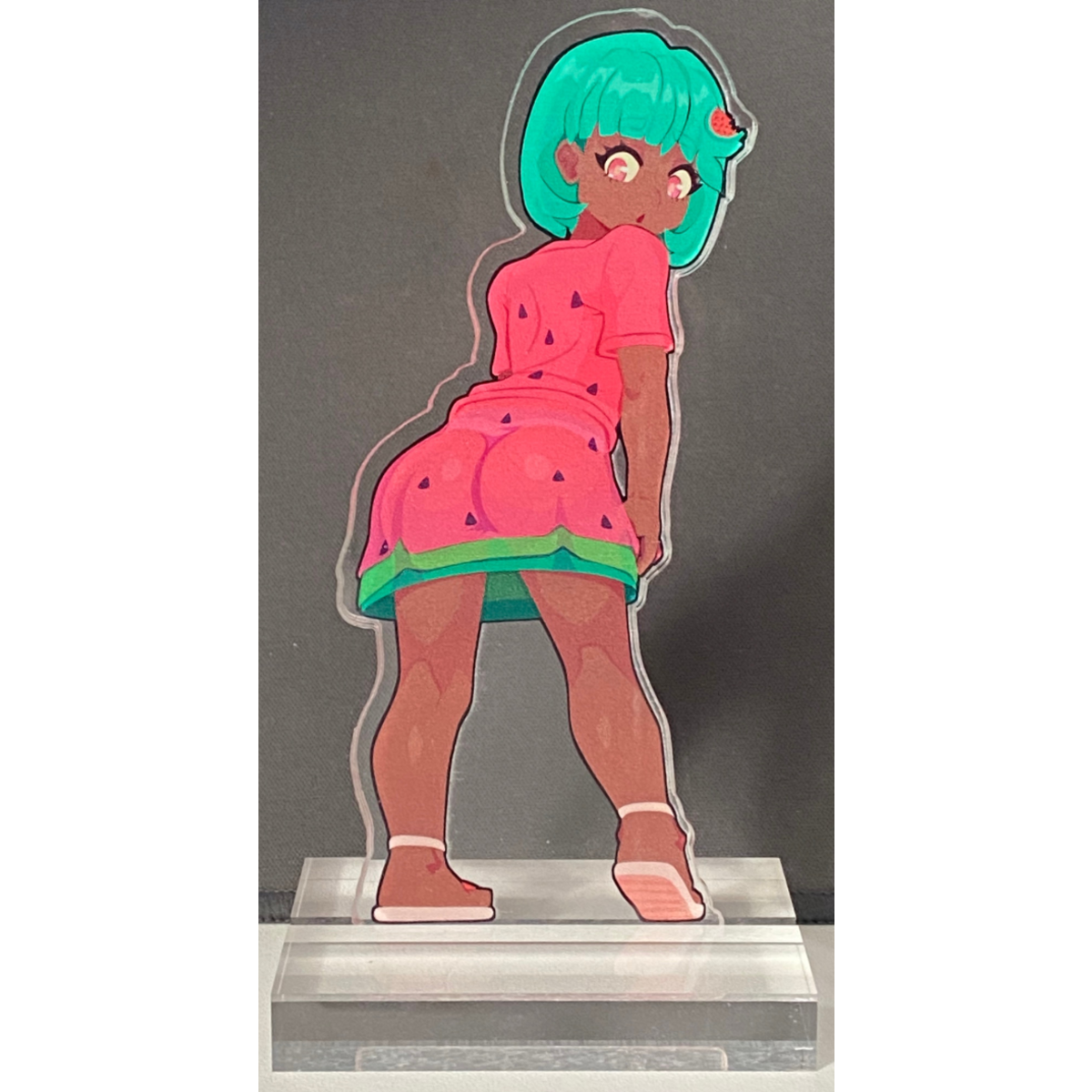 Acrylic standee of a character with green hair and watermelon-themed outfit on a gray background
